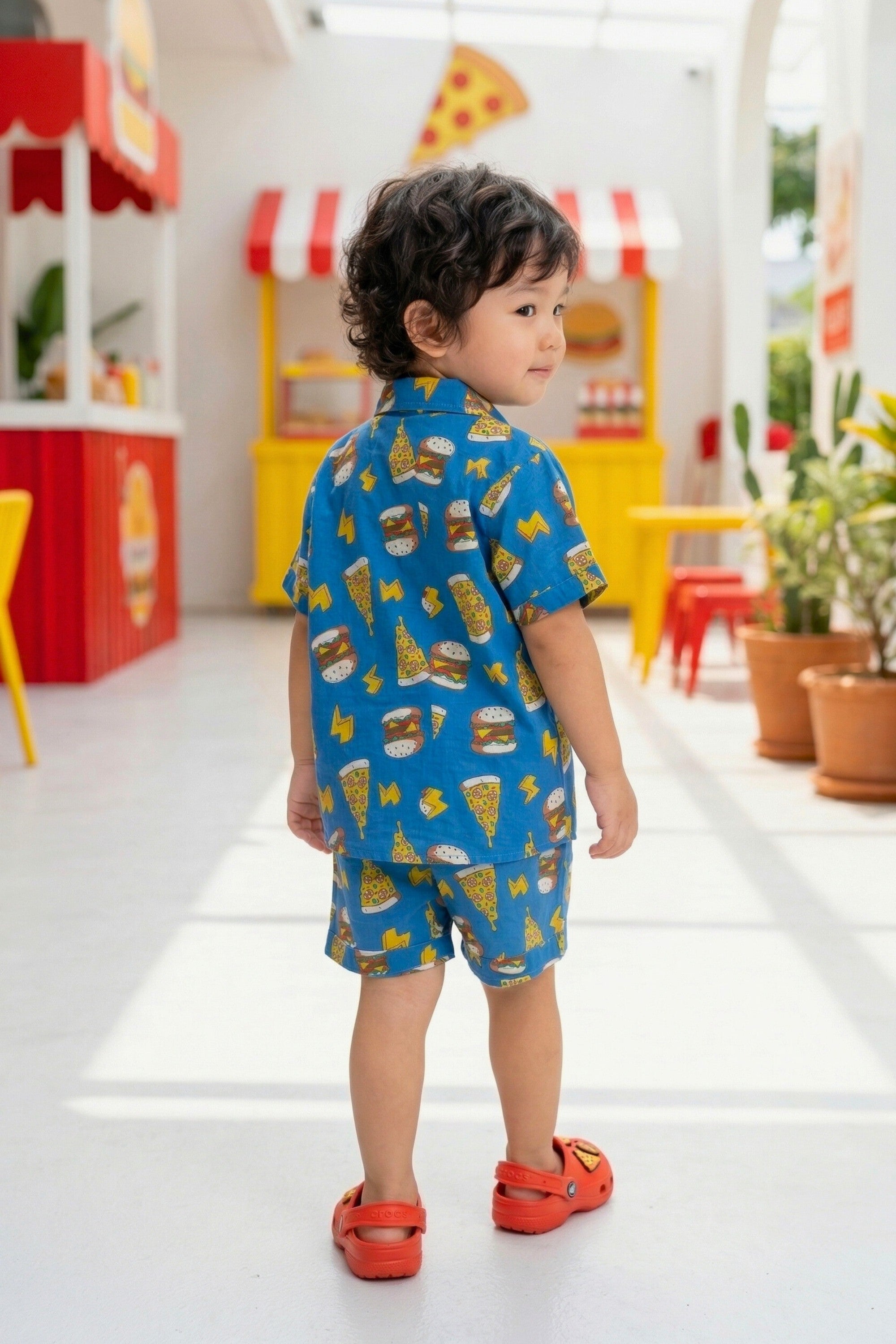 Close-up detail of the fast food doodle print on the Bebe Unicorn boys royal blue coord set — bold illustrated burgers, pizza slices and yellow lightning bolts in a graphic pop-art comic style on 100% cotton fabric for children aged 2–8 years.