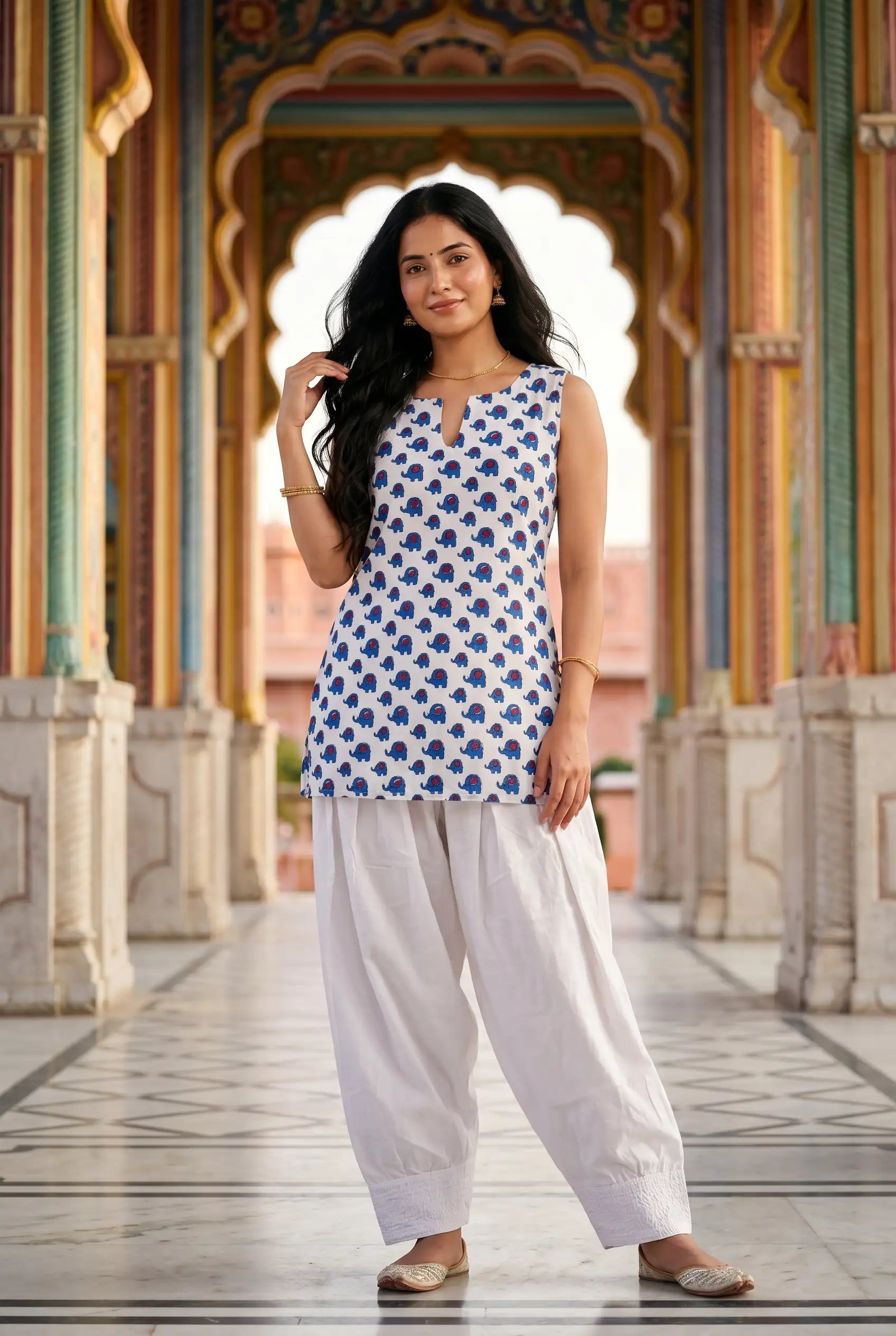 Women wearing white elephant print sleeveless kurta with farshi salwar and gold jhumkas in traditional Indian setting