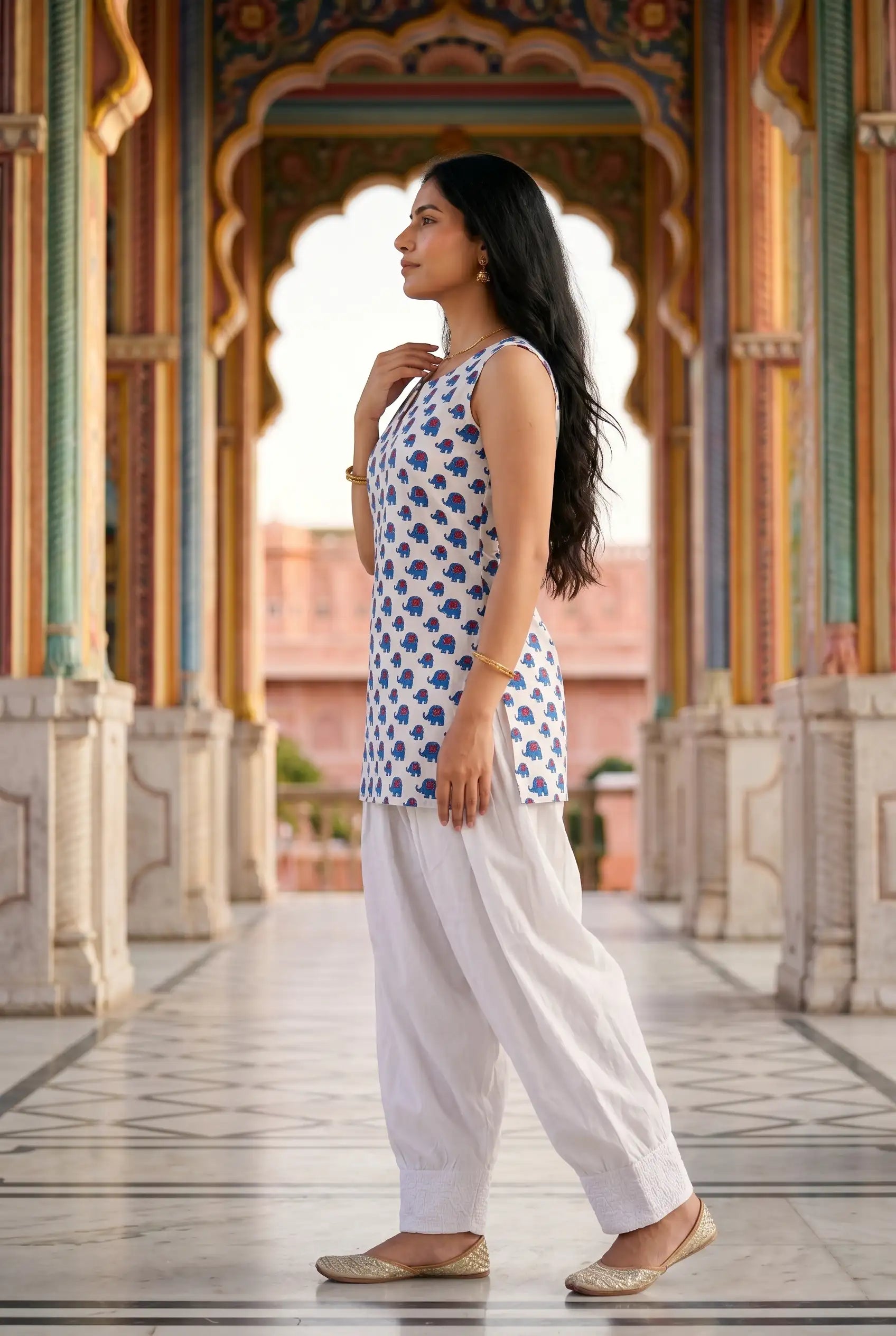 Side profile view of women's kurta farshi salwar set showing flowing silhouette with embroidered juttis at heritage location