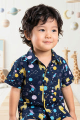 Close-up detail of the space giraffe print on the Bebe Unicorn boys navy coord set — golden amber illustrated giraffes floating through space alongside colourful planets, shooting rockets and constellation dot patterns on deep navy 100% cotton fabric for children aged 2–8 years