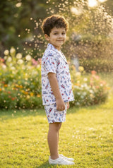 Image 4 — Print close-up / fabric detail:
Close-up detail of the surf and beach woody car print on the Bebe Unicorn 100% linen boys coord set — vintage woody station wagons with surfboards, palm trees, hibiscus flowers and starfish in red and blue on white linen, showing the natural texture of the linen fabric.