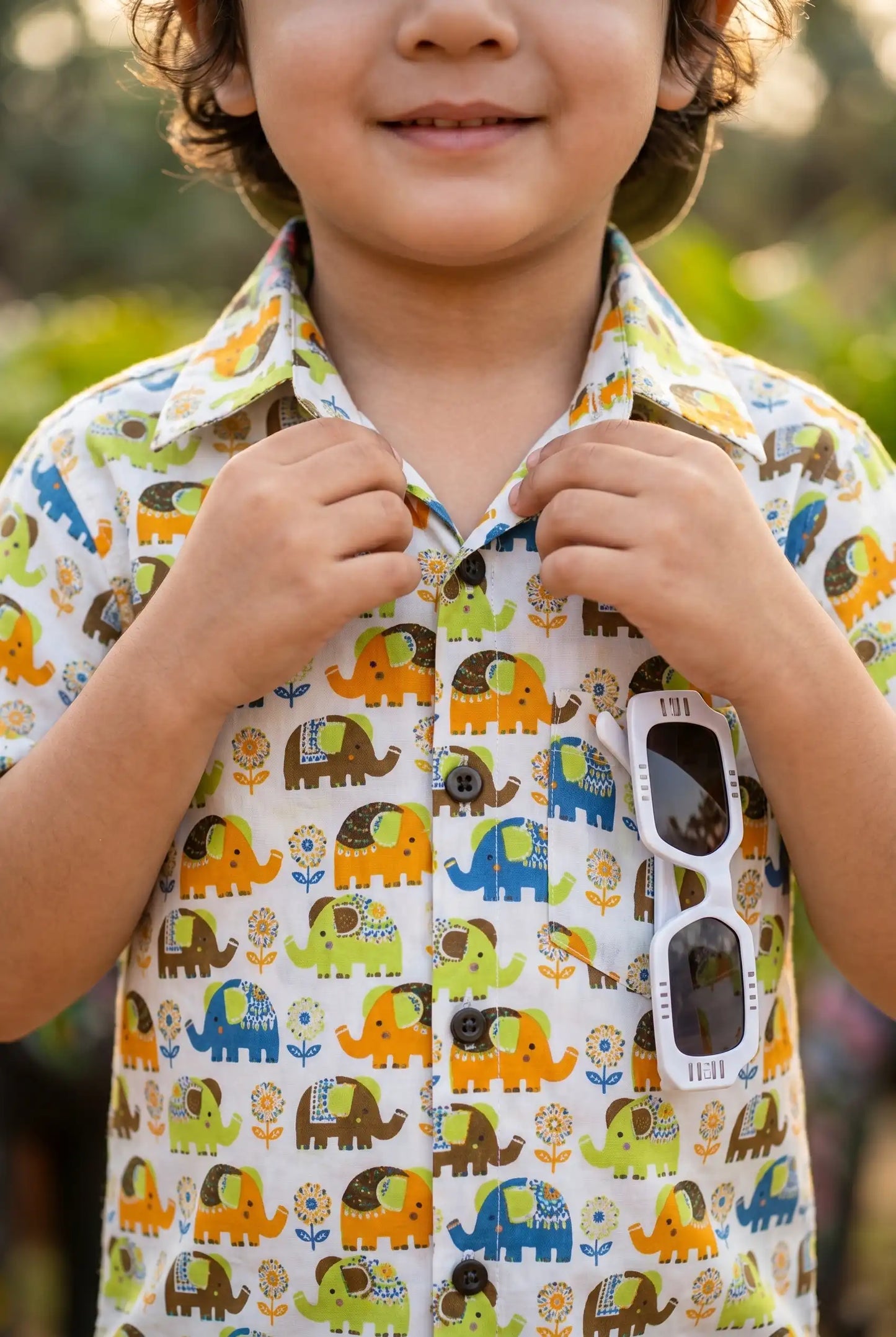 Detailed view of colorful elephant & flower print on boys casual shirt, orange blue green yellow elephants on white cotton, playful kid-friendly design