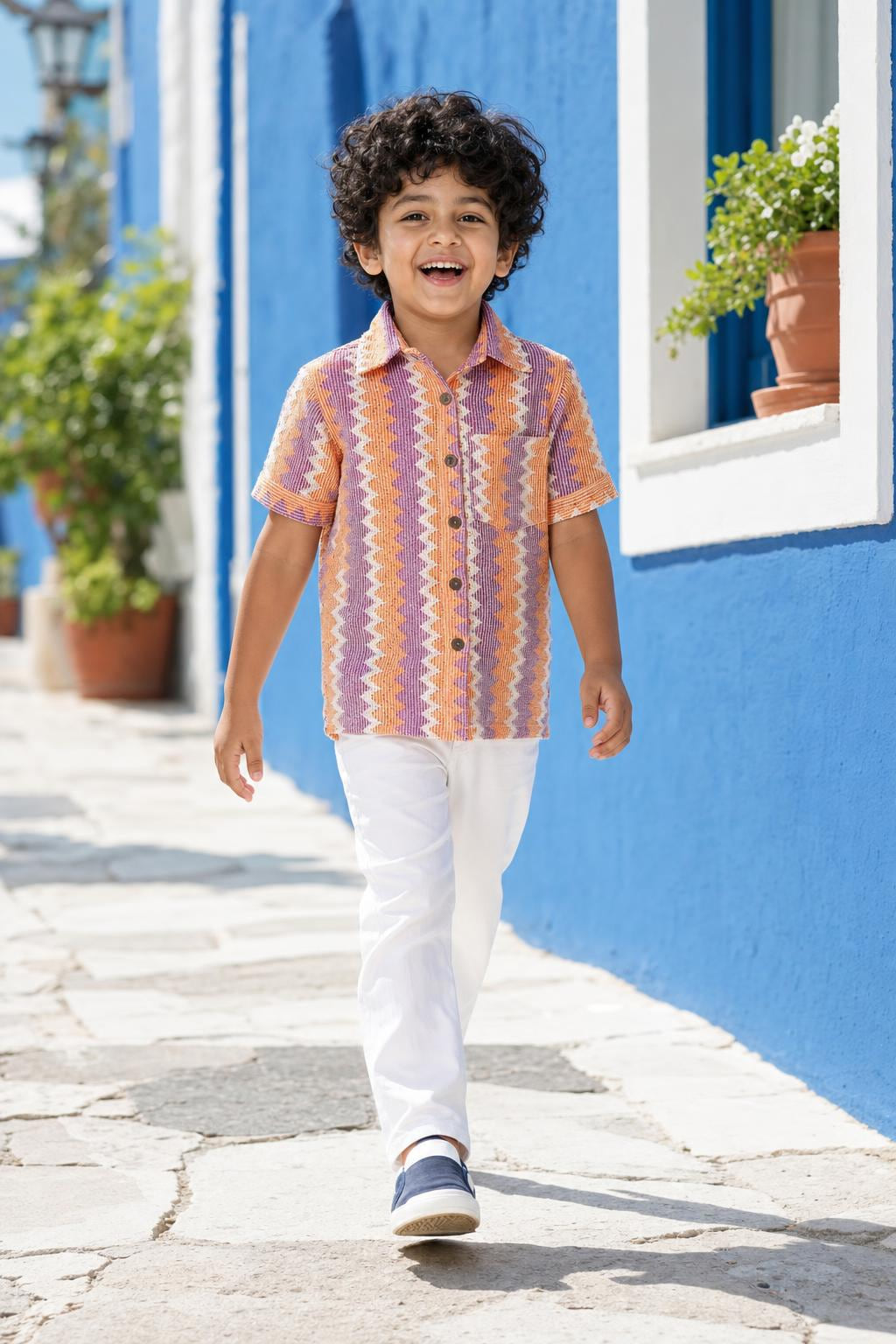 Boy wearing orange and purple zig-zag shirt with white trousers, front view