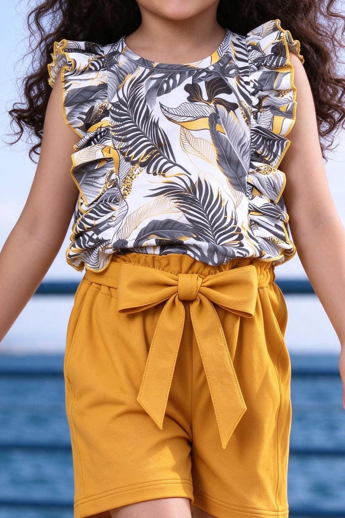 Close-up of girls floral frilled top with yellow piping and bow tie-belt shorts