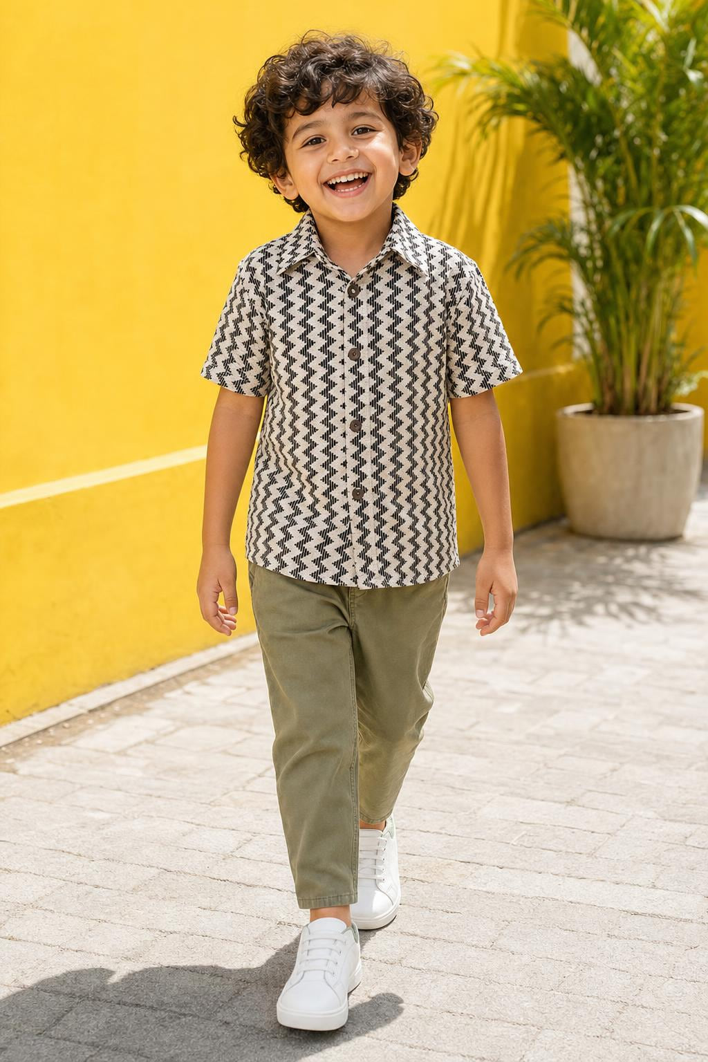 Boy wearing black and cream zig-zag print shirt with sage green chinos, front view